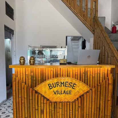 Golden bamboo counter carved with the words Burmese Village, flanked by two brass owl figurines