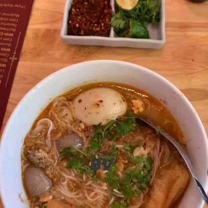 Bowl of mohinga in golden fish broth with chili flakes and sliced shallots on the side