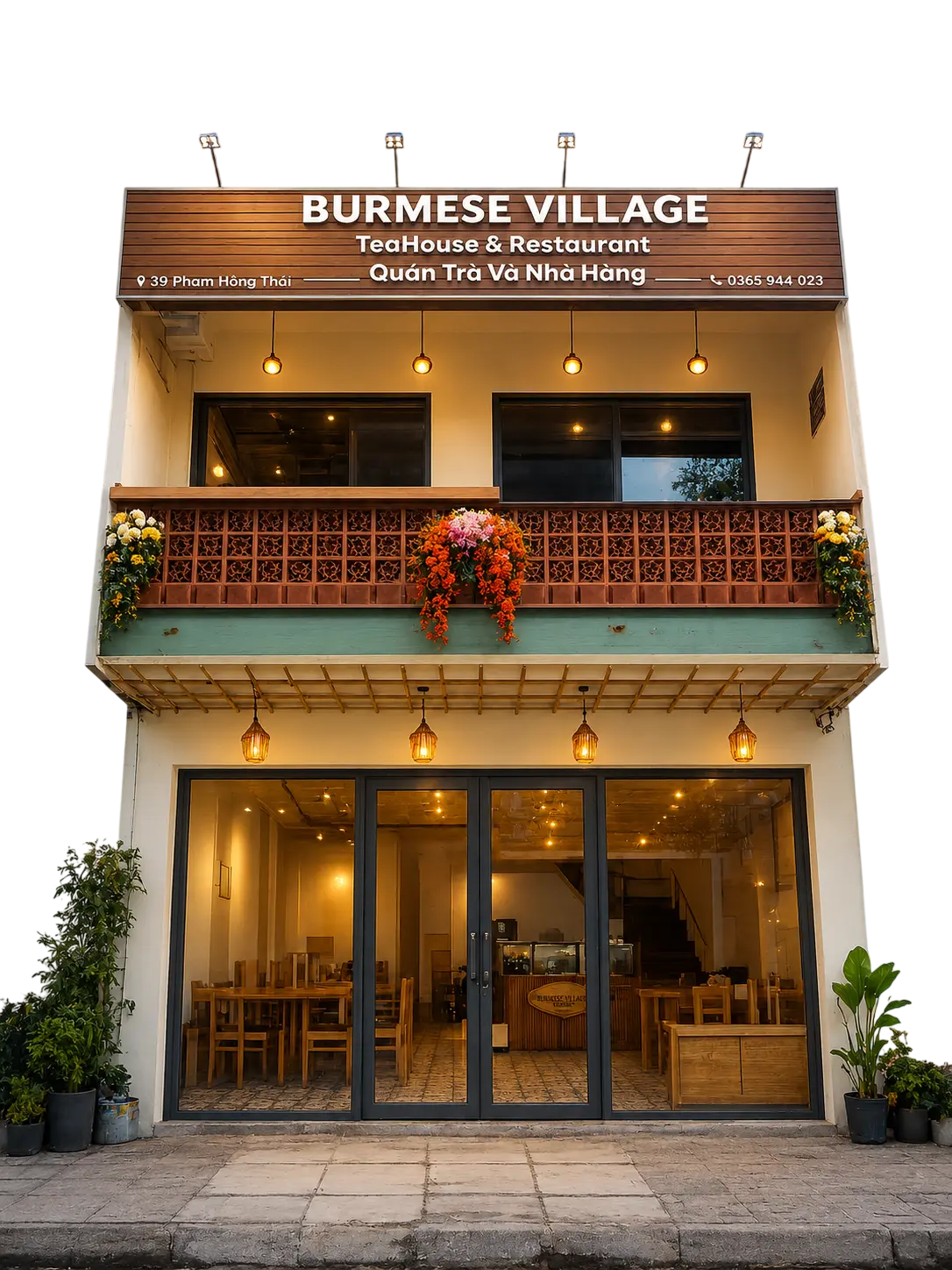 The Burmese Village building at dusk: lit sign, flowered breeze-block balcony and glowing tea-house interior