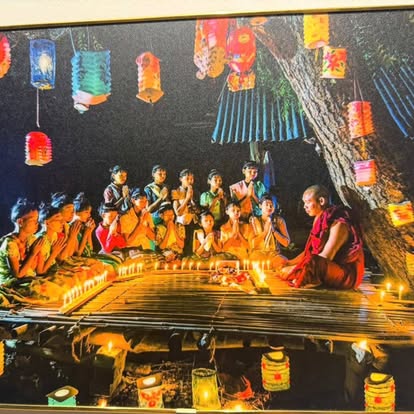 Framed photograph of children and a monk lighting candles beneath colorful paper lanterns