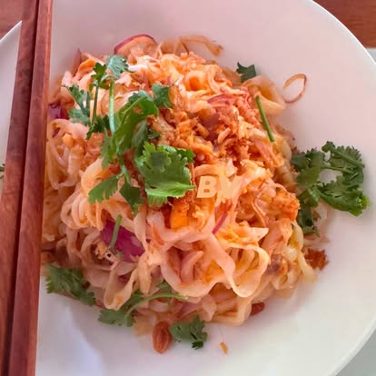 Plate of thick rice noodles hand-tossed with red onion, coriander and chili oil