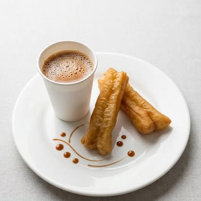 Cup of Burmese milk tea beside two golden fried dough sticks on a white plate