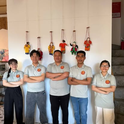 The Burmese Village crew of five in matching polos, arms crossed, marionettes on the wall behind them