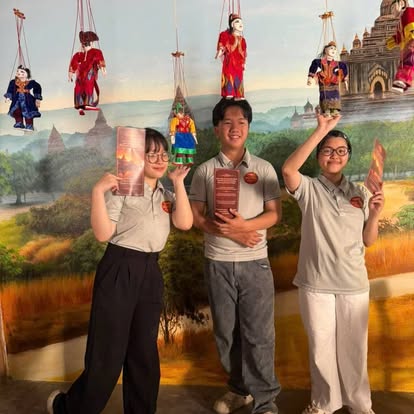 Three staff members holding menus in front of the Bagan mural, marionettes hanging above