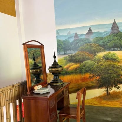 Teak dressing table with lacquered hsun ok vessels and a thanaka grinding stone, in front of a hand-painted Bagan mural